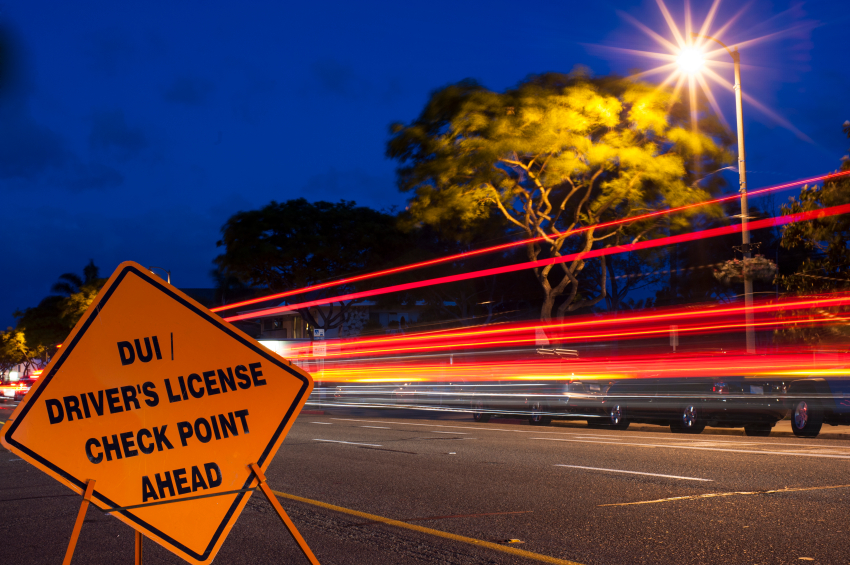 DUI / Driver license checkpoint sign with deep blue sky and car light trains in background.  Area illuminated by overhead streetlight making star.